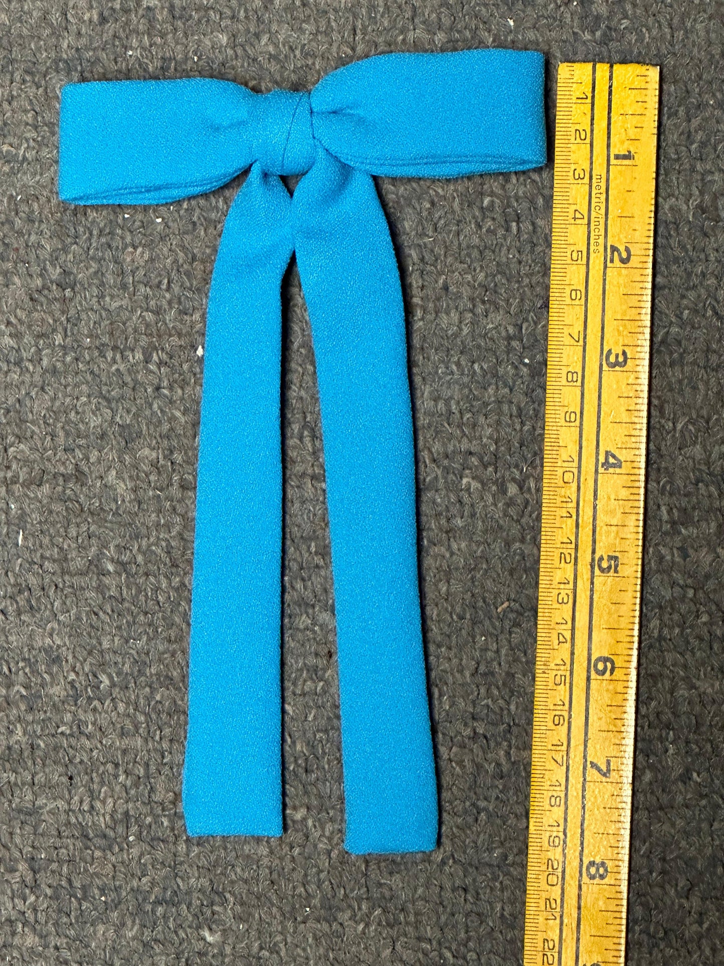 A bow tie from Square Up Fashions' Colonel Ties collection, reminiscent of southern charm, sits next to a yellow measuring tape displaying inches on a gray surface.