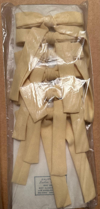 A clear plastic bag from Square Up Fashions contains several cream-colored Colonel Ties, perfectly arranged side by side on a cardboard backing, making it ideal for adding a touch of classic southern bow tie charm.