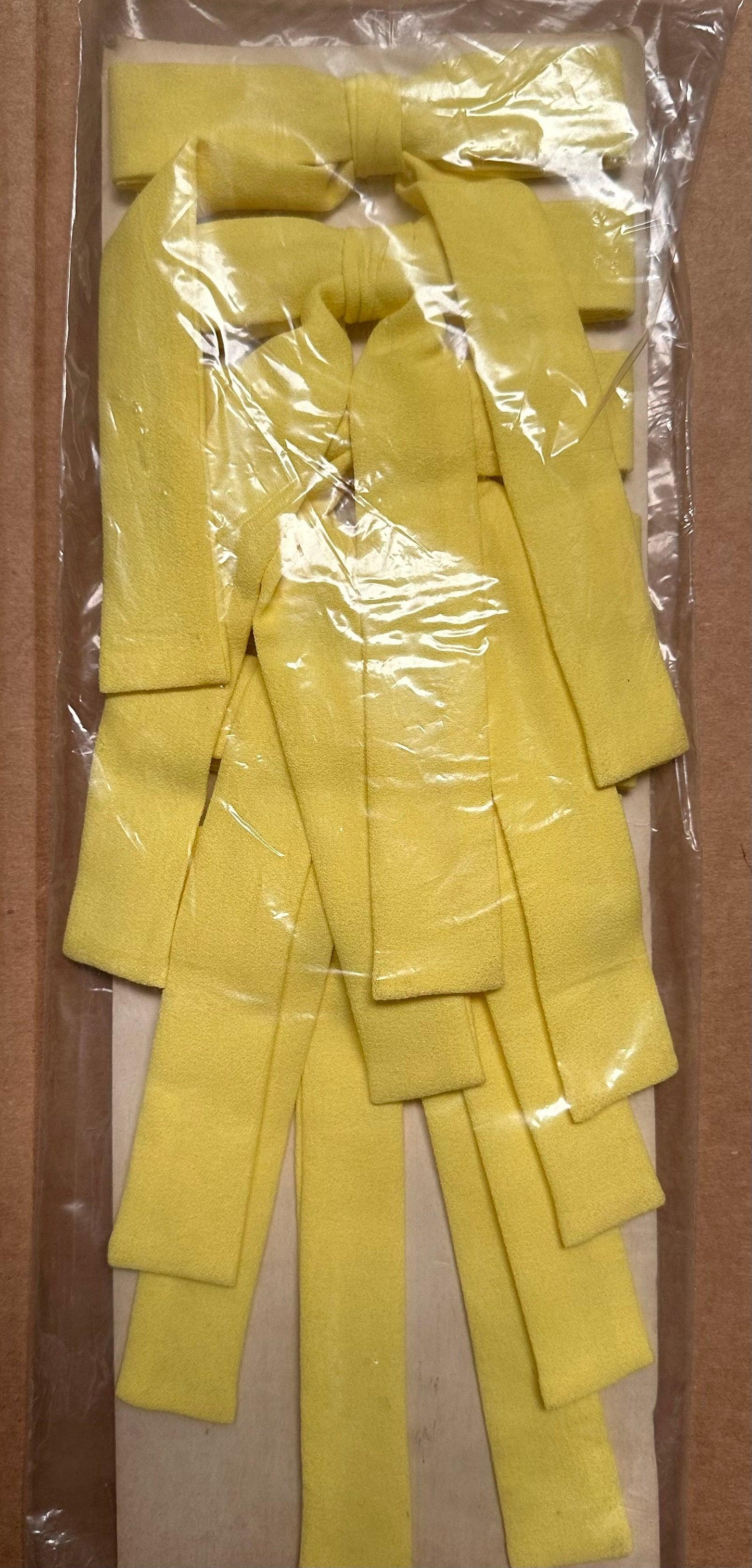 A stack of Colonel Ties in yellow, designed by Square Up Fashions, neatly arranged in plastic packaging on a cardboard backing.