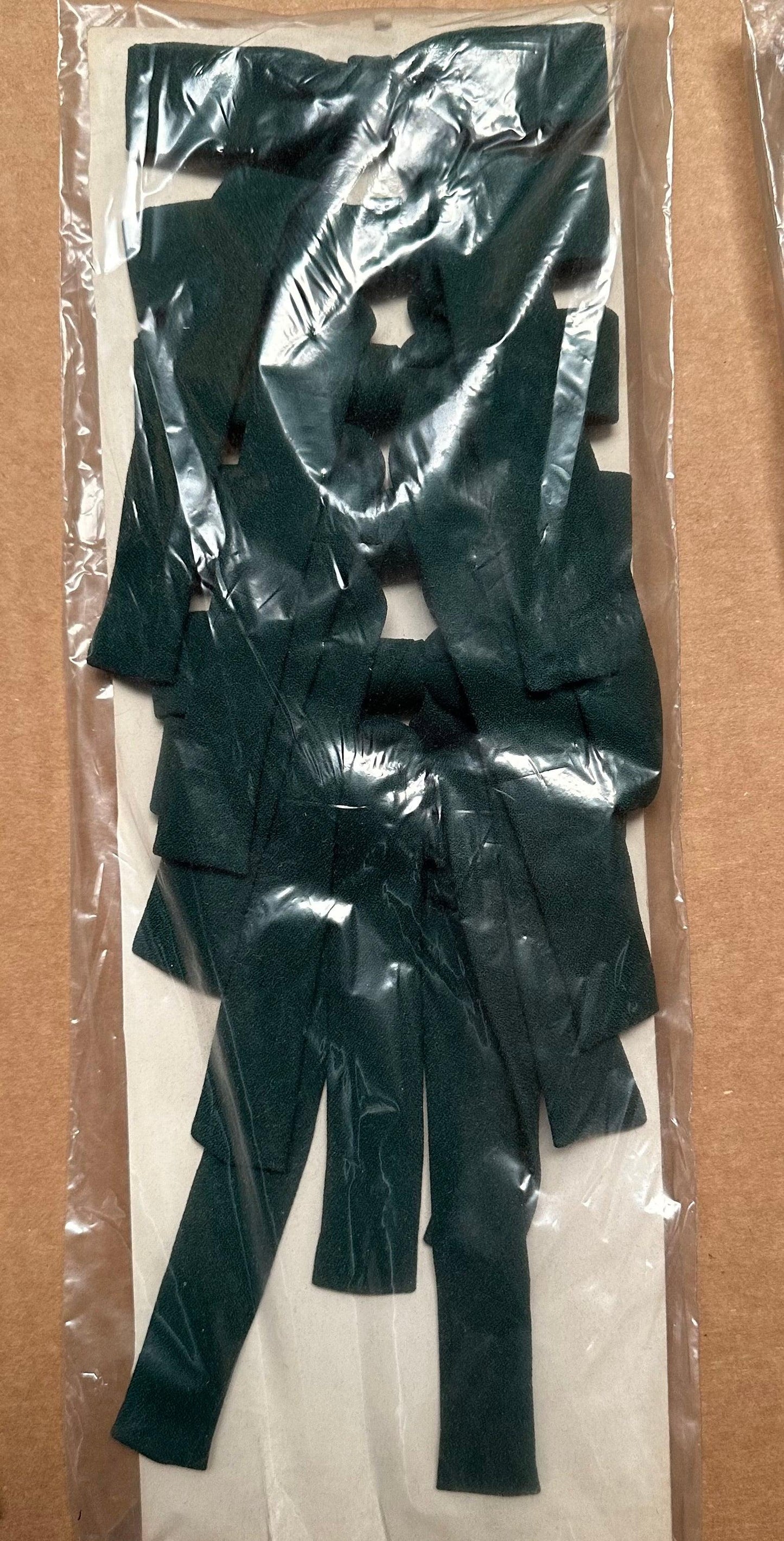 A sealed plastic bag containing multiple dark green fabric strips arranged randomly, evoking the classic appeal of Colonel Ties from Square Up Fashions, adding a southern bow tie charm to any ensemble.