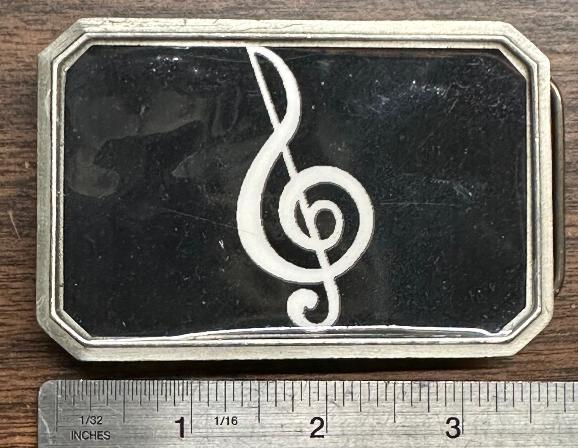The Square Up Fashions Music Note Belt Buckle is a rectangular metal accessory featuring a white treble clef on a black background, measuring about 3 inches wide.