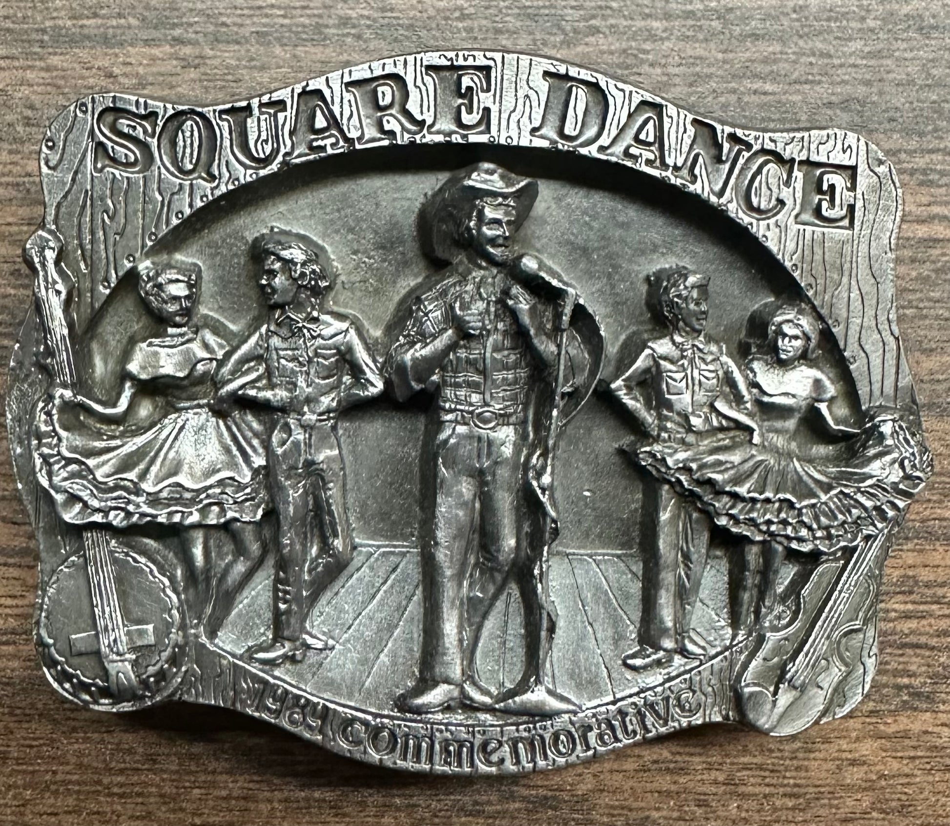 Square Up Fashions' Square Dance Buckle w/caller, made in the USA, features raised figures of a caller and four dancers on a wood floor with "Square Dance" and "The Commemorative" at the top and bottom.