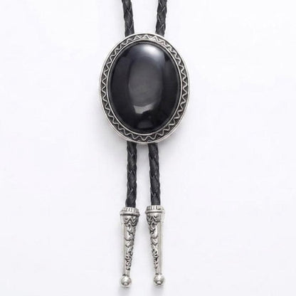 A black bolo tie necklace featuring a large oval black onyx cabochon stone surrounded by a silver-toned geometric bezel, with braided black cords and silver-toned decorative tip connectors.