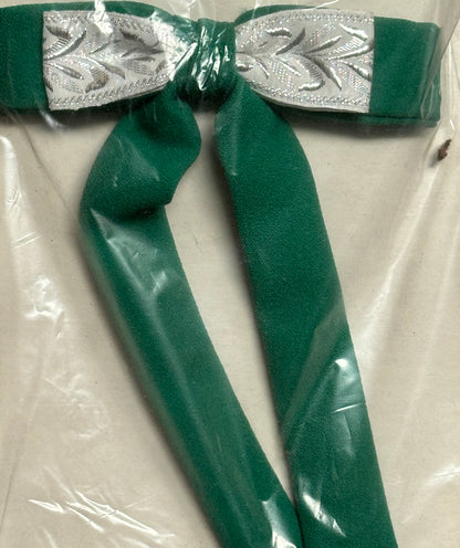 A Colonel Ties accessory, crafted by Square Up Fashions, featuring a green cloth bow adorned with a silver-patterned ribbon in the style of a southern bow tie, partially encased in clear plastic.