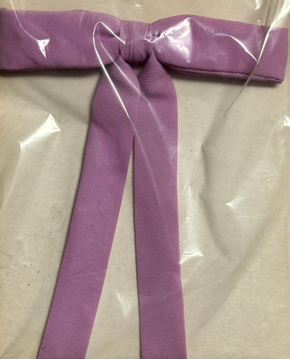 A Colonel Ties lavender fabric belt in a southern bow tie style from Square Up Fashions is showcased under clear plastic packaging on a simple background.