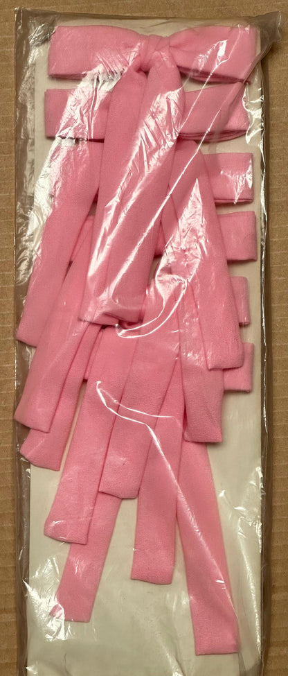 A package of Colonel Ties from Square Up Fashions, featuring pink fabric bows that evoke the style of southern bow ties, is showcased on a cardboard surface and encased in clear plastic.