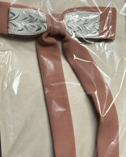 A Colonel Ties accessory by Square Up Fashions, featuring a decorative bow with a shiny silver center and long brown fabric tails, is elegantly displayed on a transparent plastic surface.