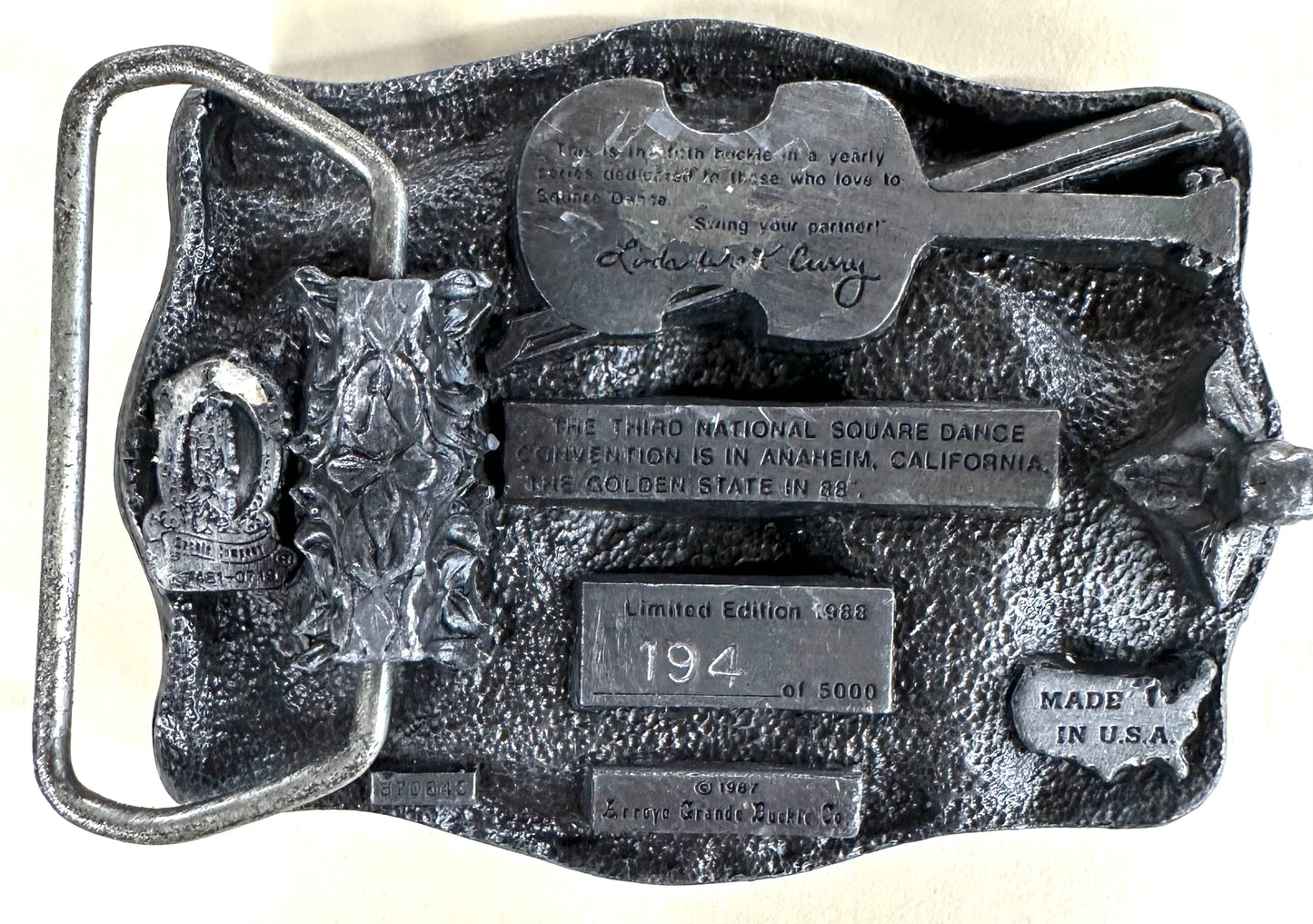 This limited edition Square Up Fashions Square Dance Buckle w/ instruments commemorates the 33rd National Square Dance Convention, 1988 Anaheim. Numbered 194 of 5000, it features a silver finish with a guitar and engraved details.