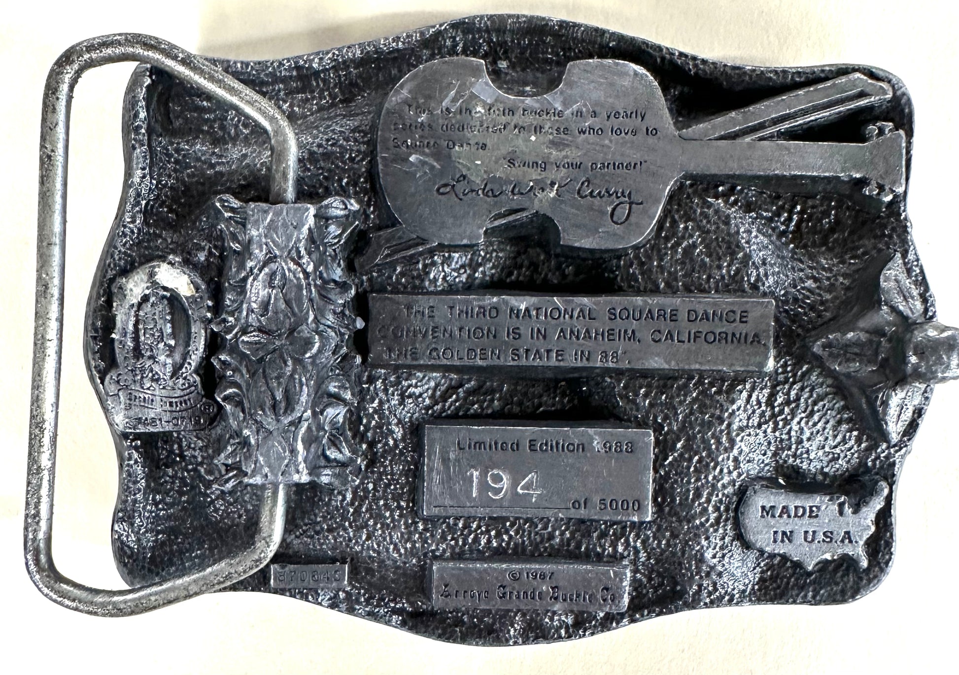 This limited edition Square Up Fashions Square Dance Buckle w/ instruments commemorates the 33rd National Square Dance Convention, 1988 Anaheim. Numbered 194 of 5000, it features a silver finish with a guitar and engraved details.