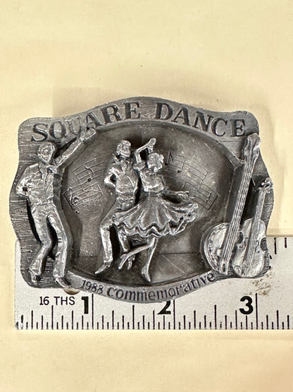 Square Up Fashions' Square Dance Buckle w/ instruments features dancers, musical notes, and a string instrument, inscribed with "Square Dance" and "1988 Commemorative"—a perfect keepsake from the 1988 Anaheim event. Shown beside a ruler for scale.