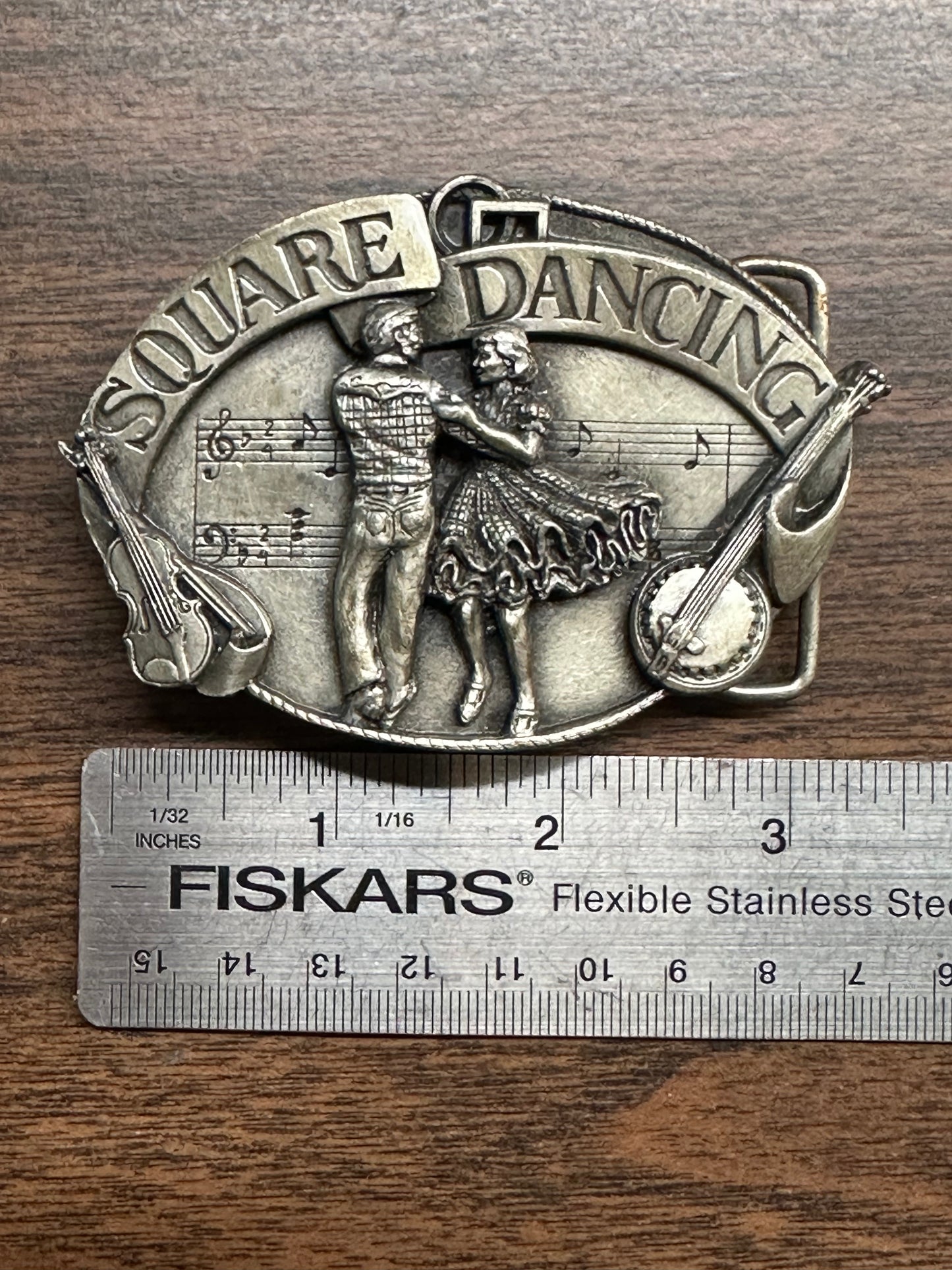 Square Dance Buckle w/ instruments by Square Up Fashions, showing a dancing couple, musical notes, and guitars with "Square Dancing" text. Measures about 3 inches wide per Fiskars ruler—1988 National square dance buckle.