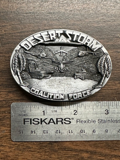 A Desert Storm Square Dance Buckle by Square Up Fashions, featuring military imagery, is shown next to a Fiskars ruler indicating it measures about 3 inches wide.