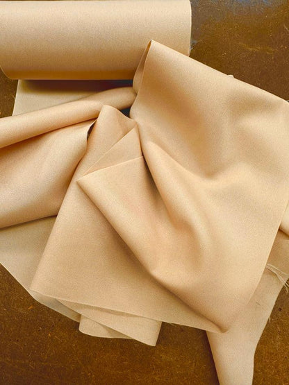 A roll of DISCOUNTED Softer Poly-Liner Petticoat by Square Up Fashions, shown in beige, is partially unrolled on a brown surface, with the soft fabric draped and folded in gentle shapes. Available in 5 colors!.